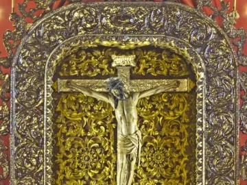 Cristo de La Laguna on the cross בתוך an ornate golden altar shrine with flowers below.