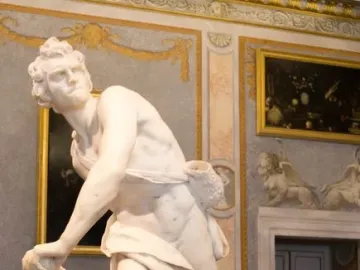 David marble statue in a gilded gallery, shown in a dynamic twisting pose with sling and draped cloth.