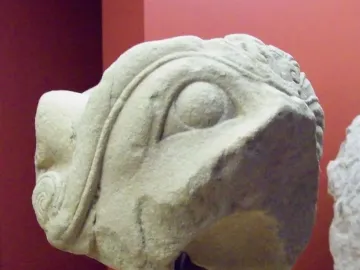 Weathered stone fragment of the Grifo de Redován showing a large round eye and ornate swirling details.