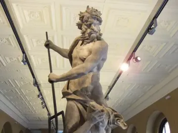 Neptune and Triton marble sculpture with a standing bearded figure holding a staff above a kneeling figure covering their face.