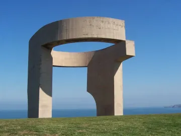 Elogio del Horizonte, a large concrete sculpture with a curved opening, standing on a grassy slope above the sea.
