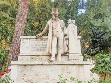 Monument to Giuseppe Gioachino Belli showing a stone statue of a man in a top hat and long coat leaning on a plinth with a cane.