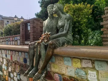 The Muretto of Alassio lovers statue, a bronze couple seated on a wall covered with colorful ceramic tiles and signatures.