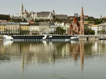 Shoes on the Danube Bank memorial along a riverside embankment, with a city skyline and riverboat in the background.