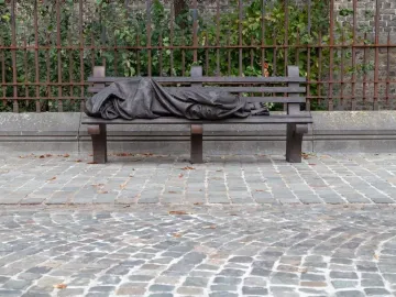 Homeless Jesus sculpture showing a sleeping figure covered by a blanket on a park bench, with wounded feet visible.