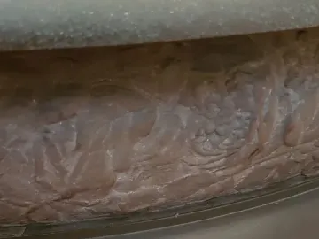 Close-up of Le Miroir showing a dark sculpted base with intricate relief patterns and a rounded edge resting on a wooden surface.