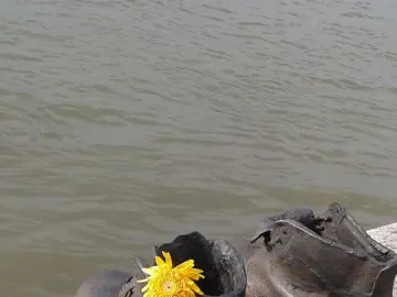 Shoes on the Danube Bank sculpture with two dark metal shoes on a concrete riverbank, one holding a yellow flower.