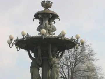Bartholdi Fountain in a snowy park with a domed building visible through bare trees