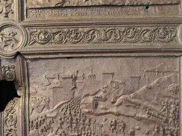 Close-up of the Bronze Gate showing a bas-relief battle scene with soldiers, horses, and a fortified city.