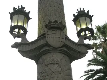 Galceran Marquet Monument detail showing a crowned coat of arms, heraldic reliefs, and two ornate lamps on ship-prow supports.