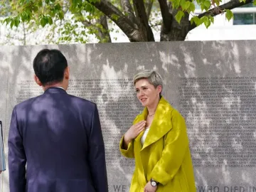 Three people stand in front of the Japanese American Memorial to Patriotism During World War II, beside a stone wall engraved with names under leafy tree branches.