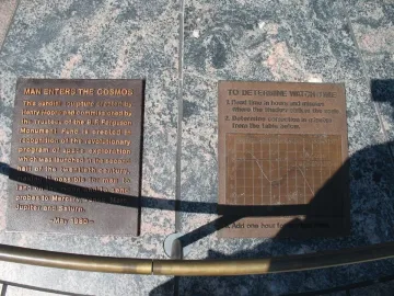 Two bronze explanatory plaques set into dark granite, with strong shadows across the surface.