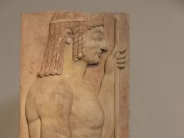 Parian Marble funerary stele of a young javelin-bearer carved in pale stone, shown in profile with curly hair and a staff.