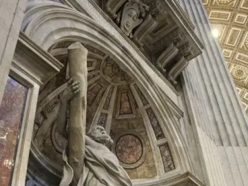 Saint Andrew stone sculpture in an ornate arched niche, holding a rough wooden post.