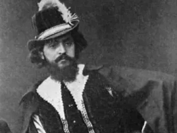 A black-and-white portrait of a man in elaborate theatrical costume with a feathered hat, ruffled collar, beard, and sword.