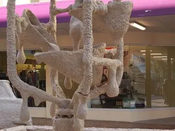 The Bucket Fountain sculpture with a rough off-white textured surface, bucket-like forms, and hanging drips, with part of a similarly covered car visible beside it.