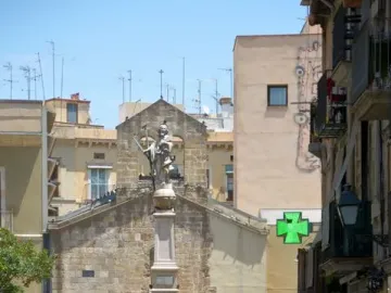 Font de Santa Eulàlia, a tall stone fountain monument in a city square with people seated around its base.