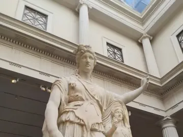 Hope Dionysus, a white marble statue of a standing classical figure with a raised left arm beside a smaller draped figure in a museum gallery.