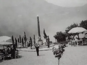 Lighthouse of Lierna standing by Lake Como with people gathered around it and mountains in the distance.