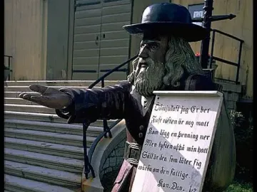 Rosenbom, a wooden statue of an old man with a beard and dark hat holding a sign across his chest.