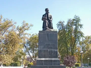 Vuk Karadžić Monument with a seated bronze figure holding a book on a tall stone pedestal surrounded by trees