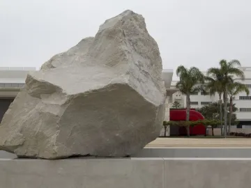 Levitated Mass boulder at LACMA with modern buildings and palm trees behind it