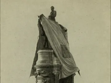 Robert E. Lee Monument with an equestrian statue atop a tall ornate pedestal, partly covered by draped fabric, with a crowd gathered below.