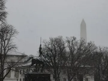 Simón Bolívar equestrian statue partly obscured by falling snow, with the Washington Monument in the background.