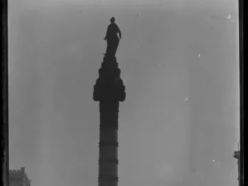 Soldiers\' and Sailors\' Monument column topped by a Liberty figure, with buildings in the background.