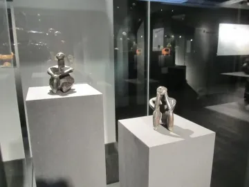 The Thinker of Cernavodă terracotta figurine displayed on a pedestal in a museum case, with a similar figure behind it.