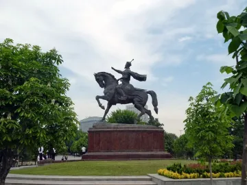 Timur Equestrian Statue on a reddish-brown pedestal in a green park with trees and flowering shrubs.