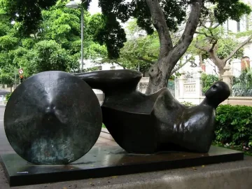 Goslar Warrior, a dark bronze reclining abstract sculpture with a circular disc on a rectangular base outdoors.