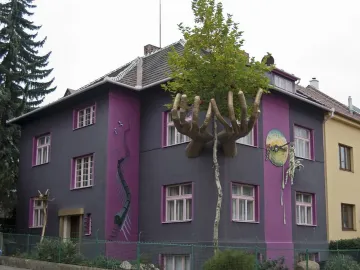 Kristek House with a dark gray facade, purple vertical stripes, golden hands, and surreal mural details.