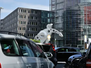 The S-Printing Horse sculpture stands beside modern buildings, partly hidden by parked cars.