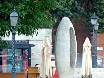 Zero Kilometre Stone sculpture beside a bed of red flowers with buildings and streetlights in the background.