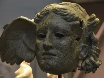 Bronze head of Hypnos with a wing on the side, showing a tranquil face with wavy hair and a weathered surface.