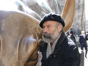 Arturo Di Modica stands beside the Charging Bull sculpture, touching its snout.