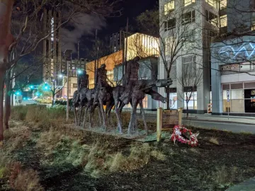 The Partisans sculpture in Boston, shown at night with figures on horseback, a memorial plaque, and a floral wreath at the base.