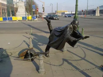 Vaartkapoen bronze statue showing a helmeted figure falling backward as another emerges from a manhole to grab their leg.