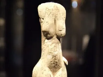 Venus of Eliseevichi carved figurine with prominent breasts and hips, shown on a support against a dark background.