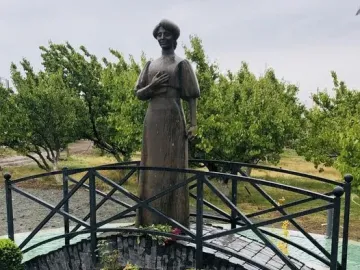 Bronze statue of Zabel Yessayan holding a book on a small arched bridge in a circular garden bed.