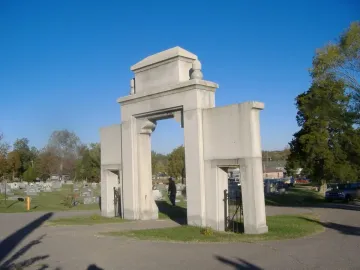 Confederate Memorial Gateway with a large central arch and two smaller side arches beside a cemetery road.