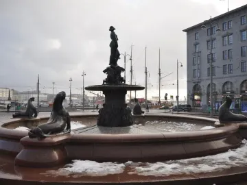 Havis Amanda fountain with a bronze female statue on a pedestal, surrounded by sea lion figures and patches of snow.