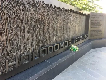 Holodomor Memorial wall with wheat stalk relief and flowers placed below the HOLODOMOR 1932-1933 inscription.
