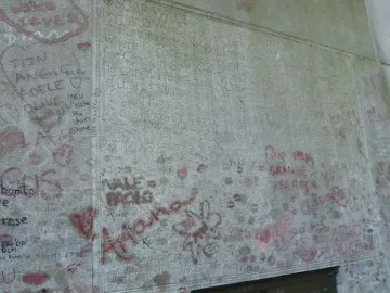 Oscar Wilde\'s tomb covered with graffiti, handwritten messages, hearts, and red lipstick kiss marks.