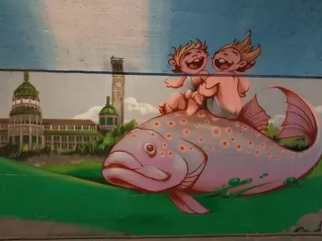 Mural inspired by the Rhine Water Fountain showing two cherubic figures riding a spotted pink fish over green hills with a city skyline behind them.