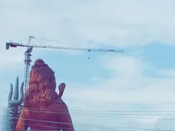 The Statue of Belief rises above scaffolding, with a crane behind it and power lines in the foreground.