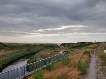 The Man by the Sea sculpture appears in the far right distance against a cloudy coastal landscape.