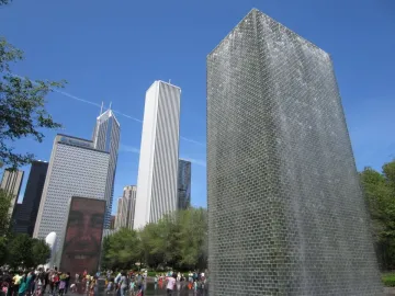 Crown Fountain with water cascading down one tower and a projected face on the other, with people gathered in the shallow pool below.