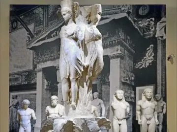 Dancers of Delphi sculpture with three draped female figures atop a textured column base.